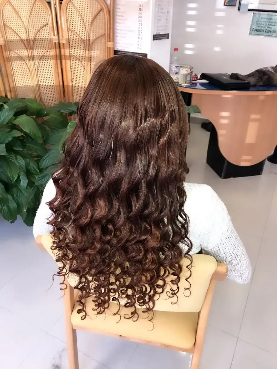 Una peluquera aplica champú mediante un masaje en el cabello oscuro de una clienta en el lavabo de la peluquería.