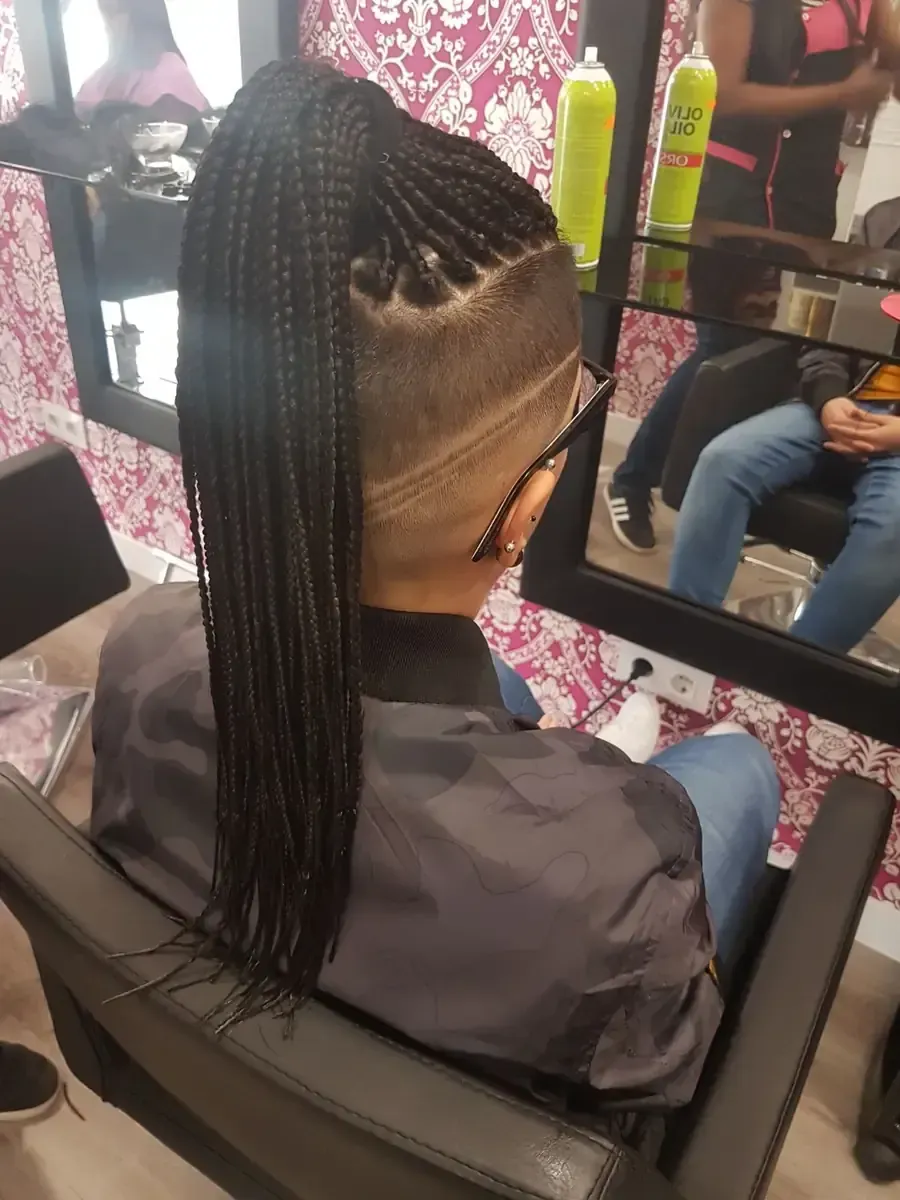 Peluquera trenzando cabello oscuro con reflejos cobrizos, usando pinzas y un peine.