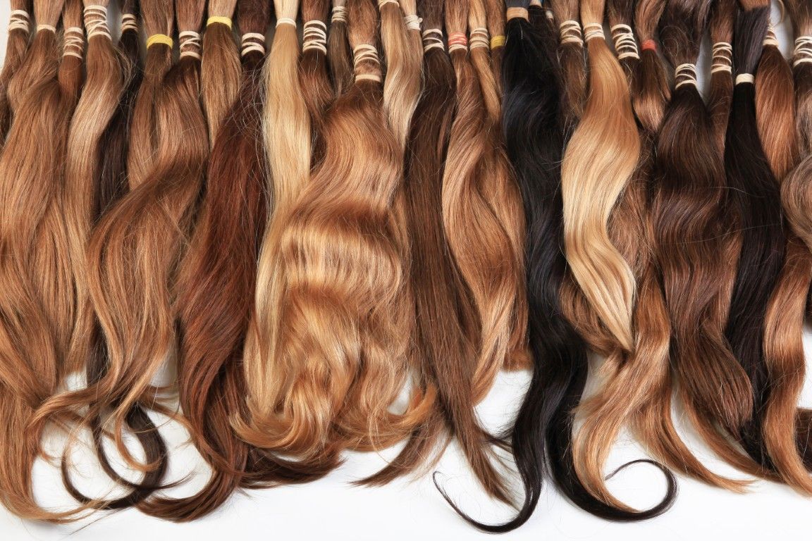 Varias extensiones de cabello ondulado, castaño y rojizo, colgadas en fila.