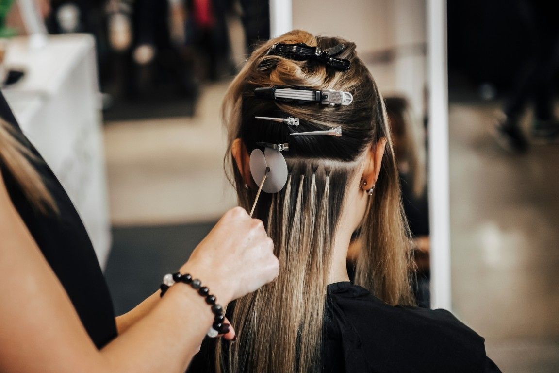 Una estilista aplica mechas con papel de aluminio en el cabello largo y castaño de una clienta en un salón de belleza.