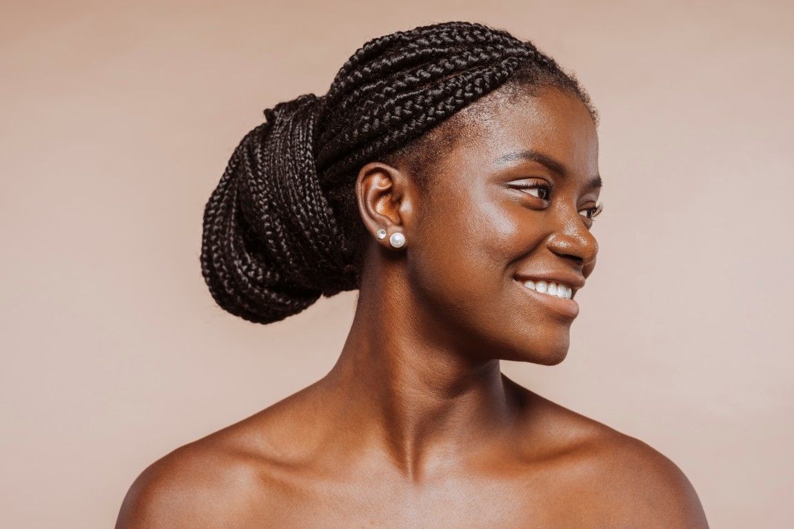 Persona sonriente con el pelo trenzado recogido en un moño bajo sobre un fondo rosa suave.