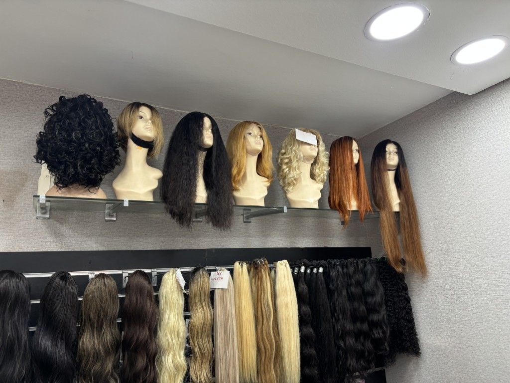 Levantando con la mano una sección de cabello largo, liso y castaño sobre un fondo claro.