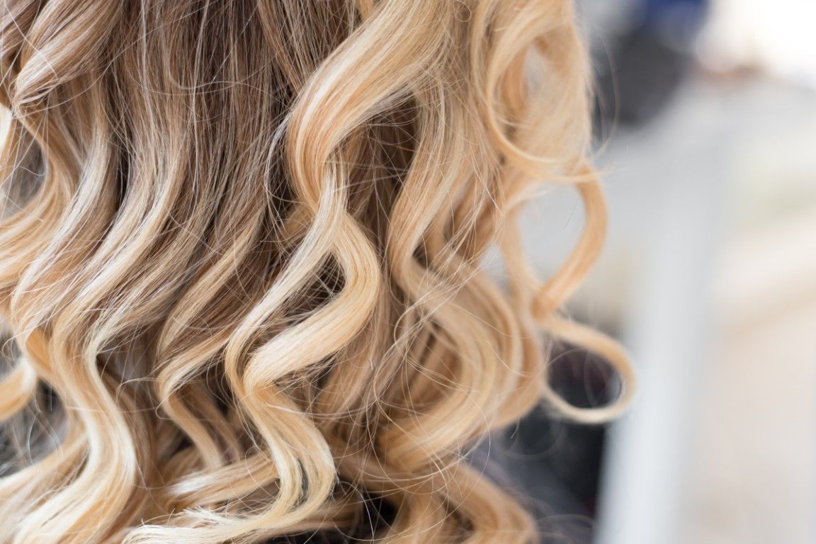 Primer plano de cabello rubio ondulado peinado en rizos sueltos con raíces oscuras.