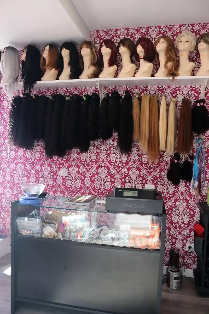 Mujer sosteniendo y examinando una extensión de cabello castaño oscuro sobre un fondo liso.