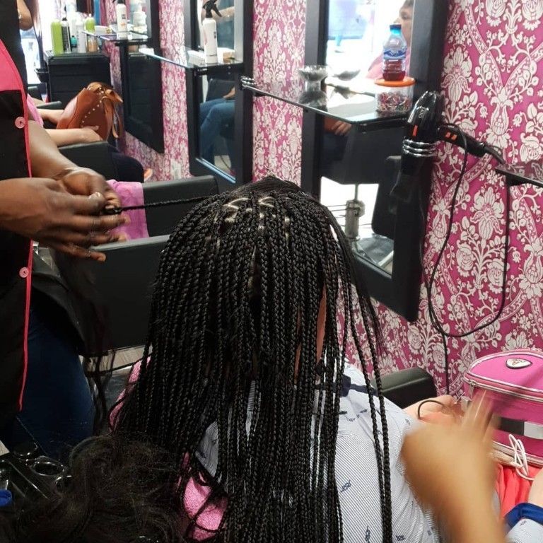 Peinado con trenzas siendo arreglado frente al espejo de una peluquería con paredes estampadas en rosa.