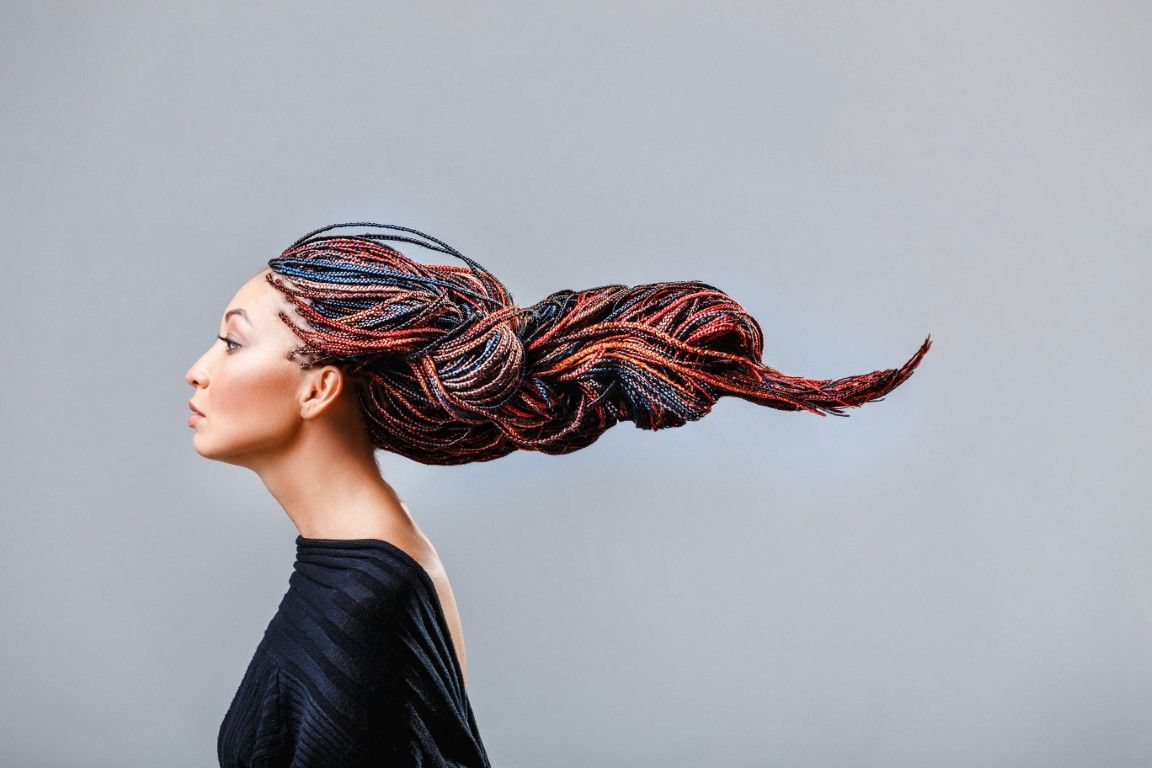 Perfil de una mujer con el cabello trenzado cayendo hacia atrás sobre un fondo gris liso.