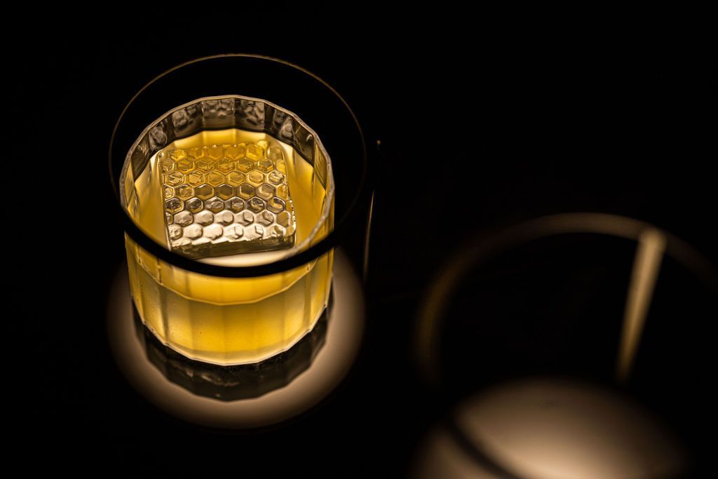 A close up of a glass of whiskey with ice on a table.