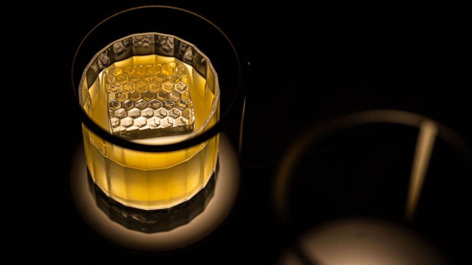 A close up of a glass of whiskey with ice cubes on a table.