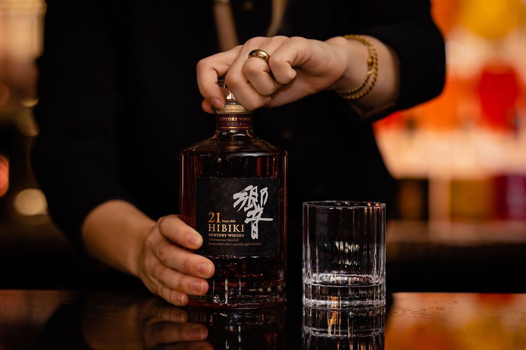 A woman is pouring a bottle of whiskey into a glass.
