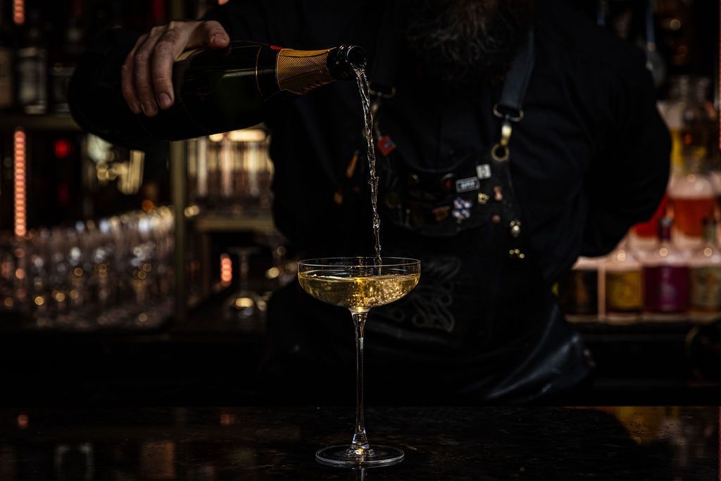 A bartender is pouring champagne into a glass at a bar.