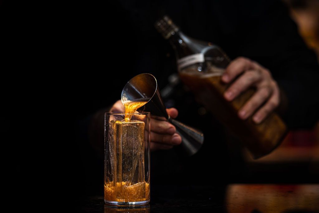 A bartender is pouring a drink from a bottle into a glass.
