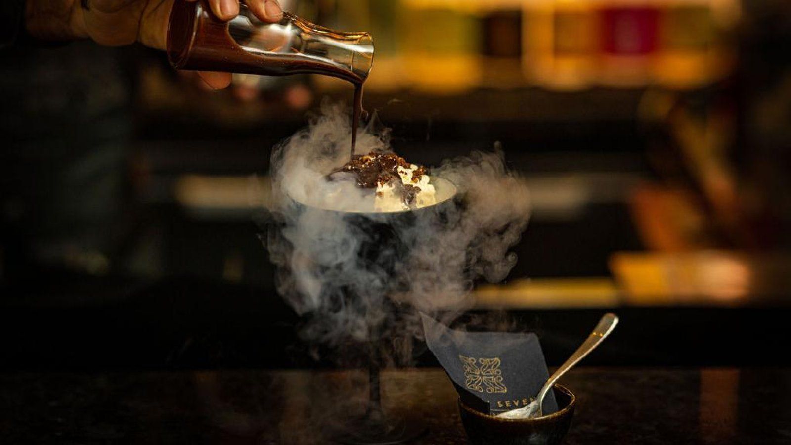 A person is pouring chocolate sauce into a bowl of ice cream.