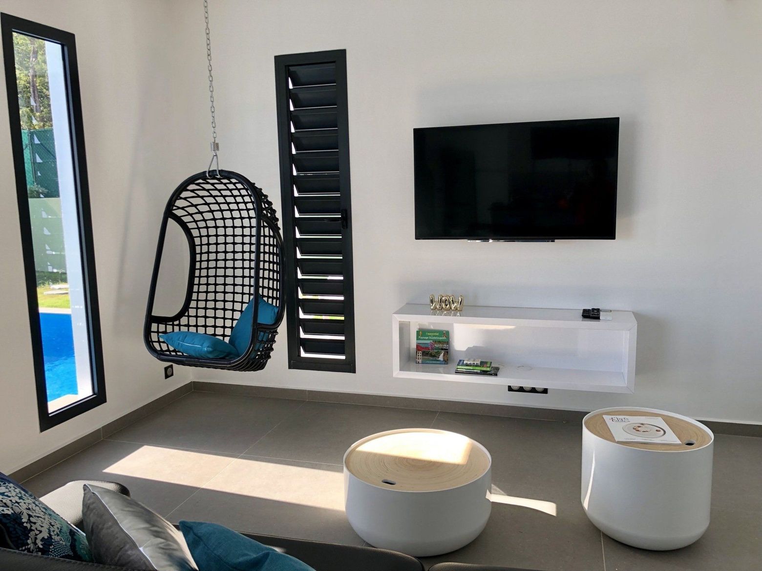 Prise de vue d'une jalousie de sécurité depuis un salon équipé d'un fauteuil et d'une télévision.