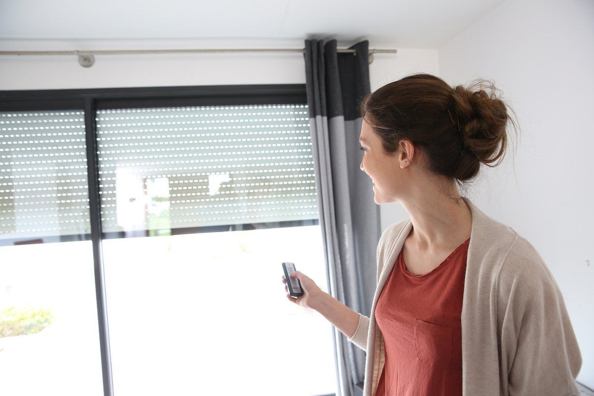 Une personne qui utilise une télécommande pour piloter l'ouverture et la fermeture de ses volets roulants.