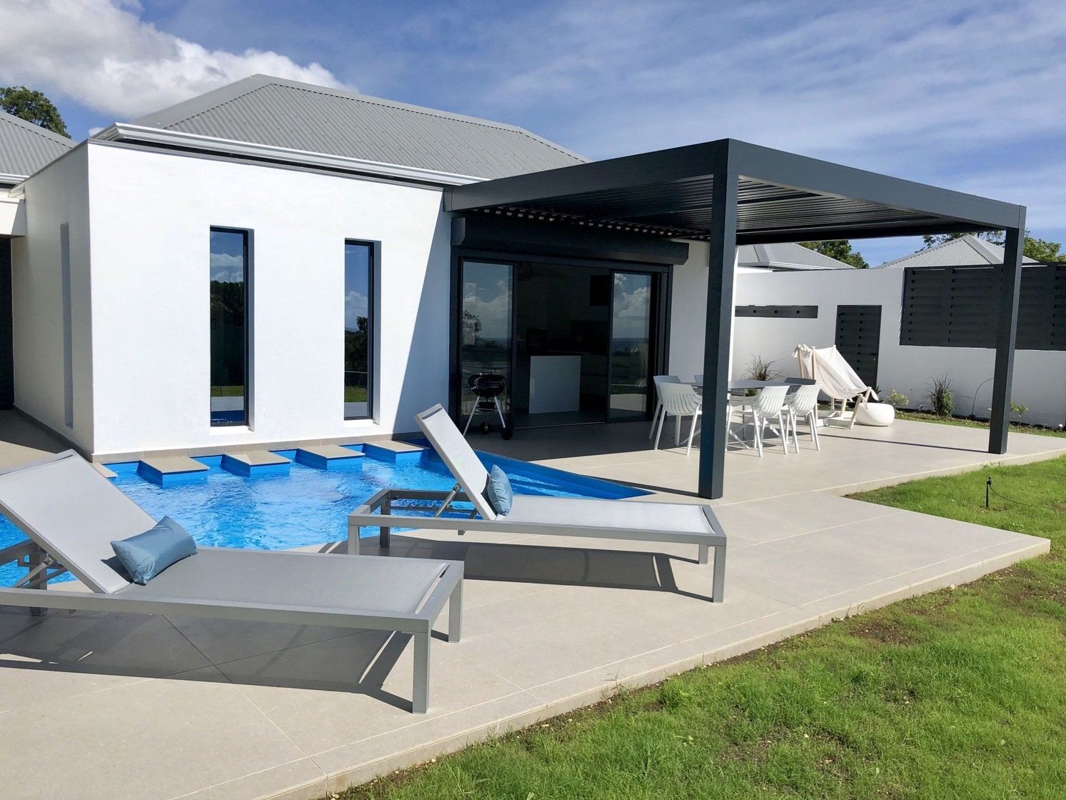 Une terrasse avec une piscine et une pergola attenante à une maison avec des fenêtres.