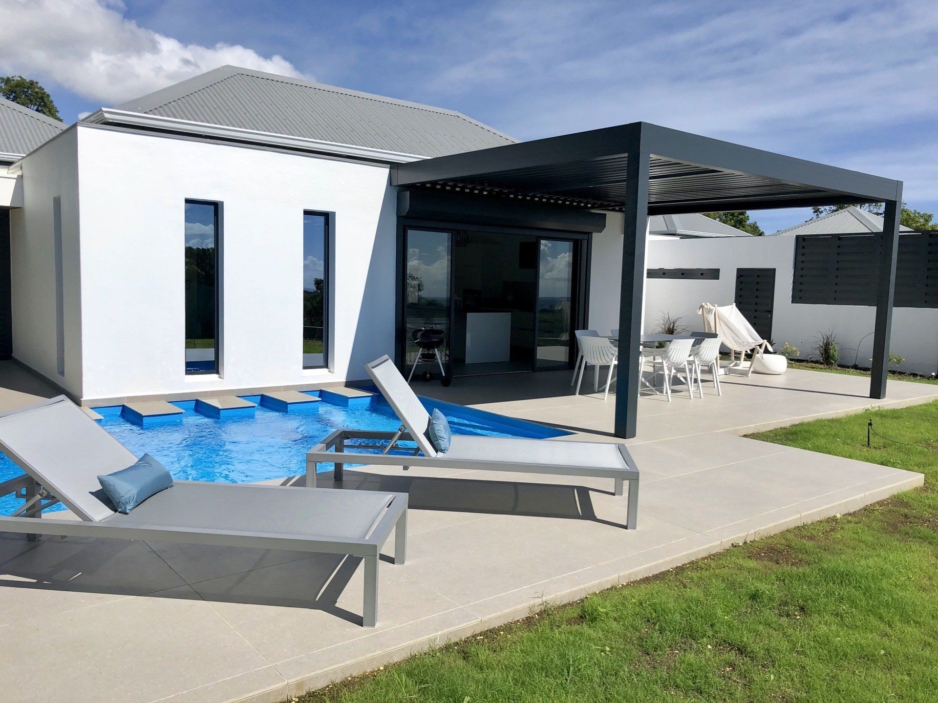 Une terrasse avec une piscine et une pergola attenante à une maison avec des fenêtres.