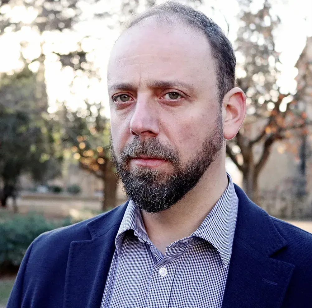 Una persona con barba, que viste una camisa estampada con cuello y un blazer azul