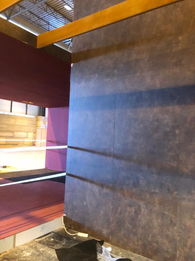 Vista interior de un edificio en construcción. Paneles de pared marrón oscuro con juntas horizontales junto a una pared rosa.