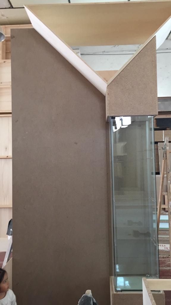 Gran estructura de aglomerado marrón con parte superior en ángulo, que cubre parcialmente un tanque de vidrio alto.