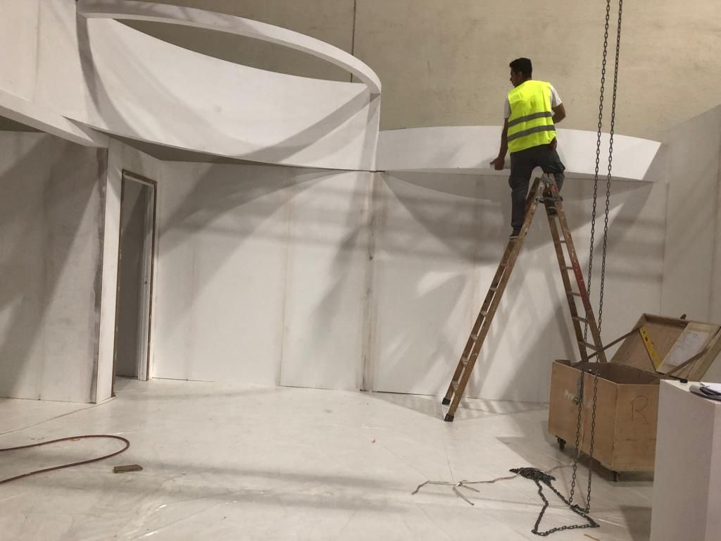 Un trabajador en una escalera instala paneles blancos en un espacio interior con un elemento de techo curvo.