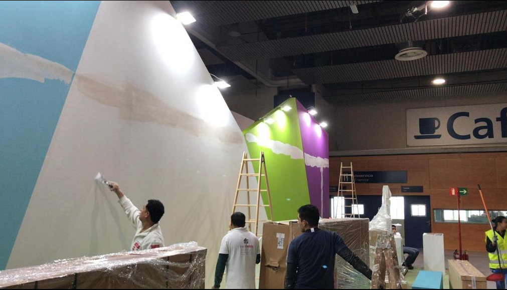 Personas pintando paredes de colores en un entorno interior, con escaleras y cajas cerca.