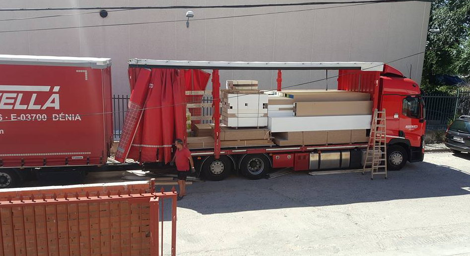 Camión rojo con remolque cargado de muebles; cortinas laterales abiertas.