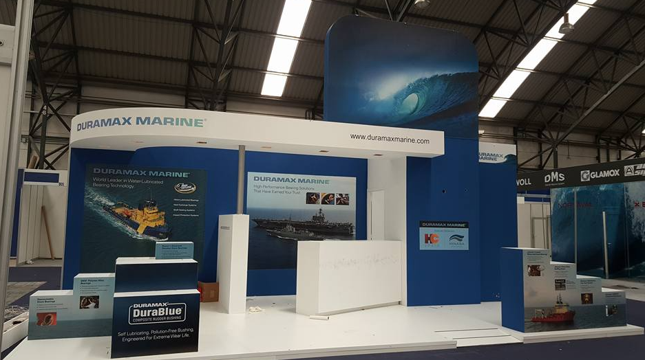 Stand de IMAX MARINE en una feria comercial con colores azul y blanco, promocionando servicios marinos; un fondo de olas del océano.