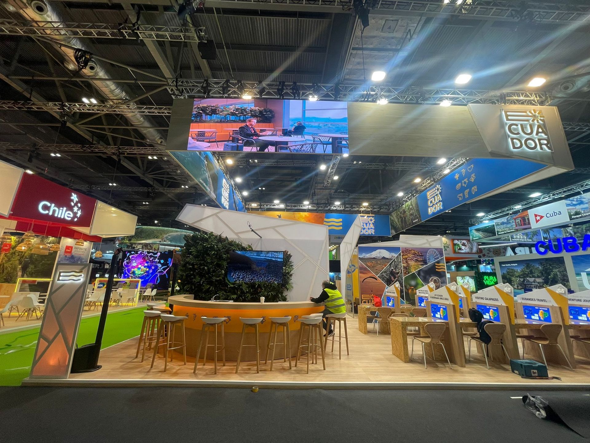 Stands de feria con pantallas digitales y asientos, que muestran diferentes países.