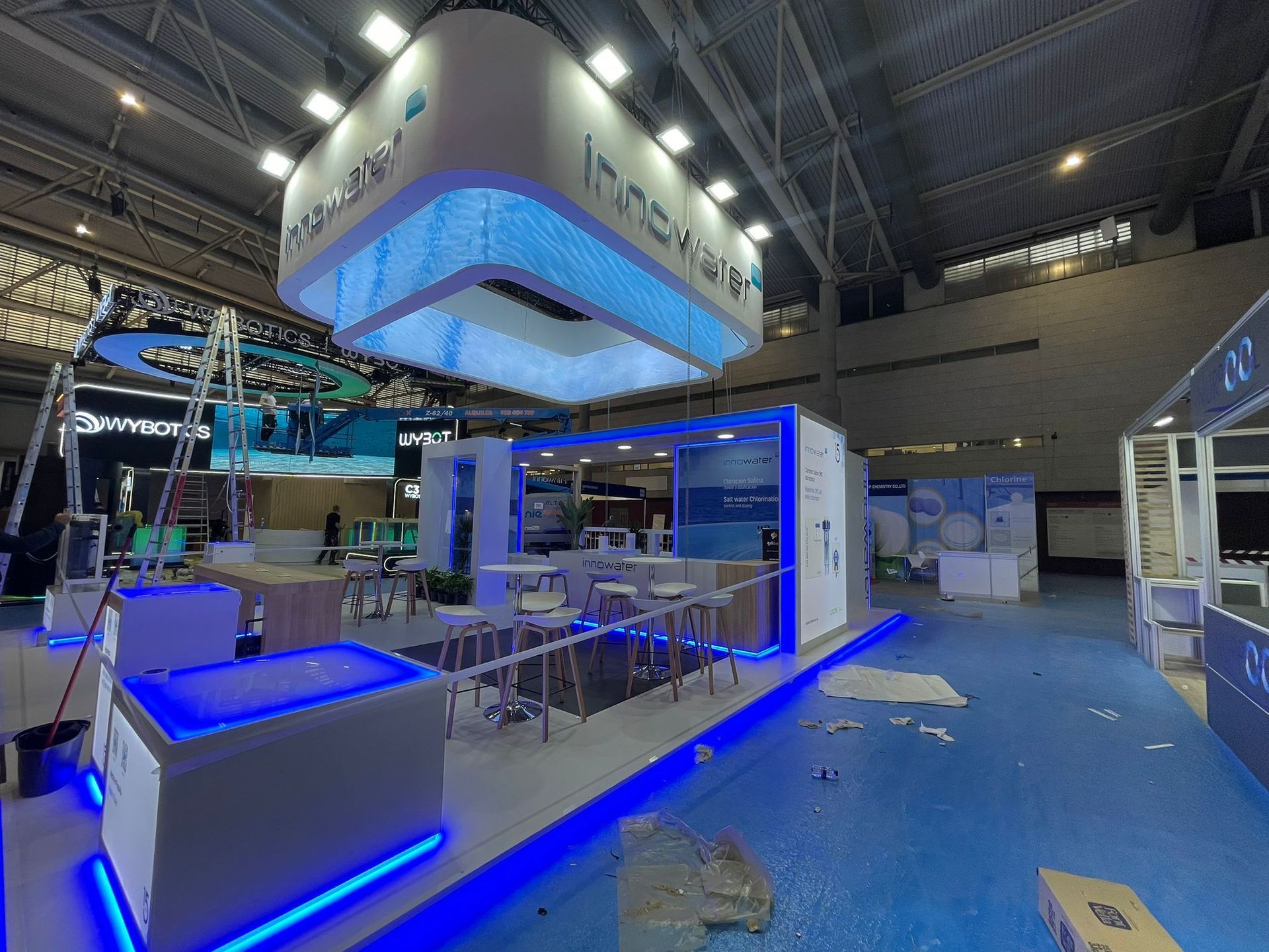 Stand de feria comercial con cartel colgante, detalles en azul y blanco y suelo reflectante.