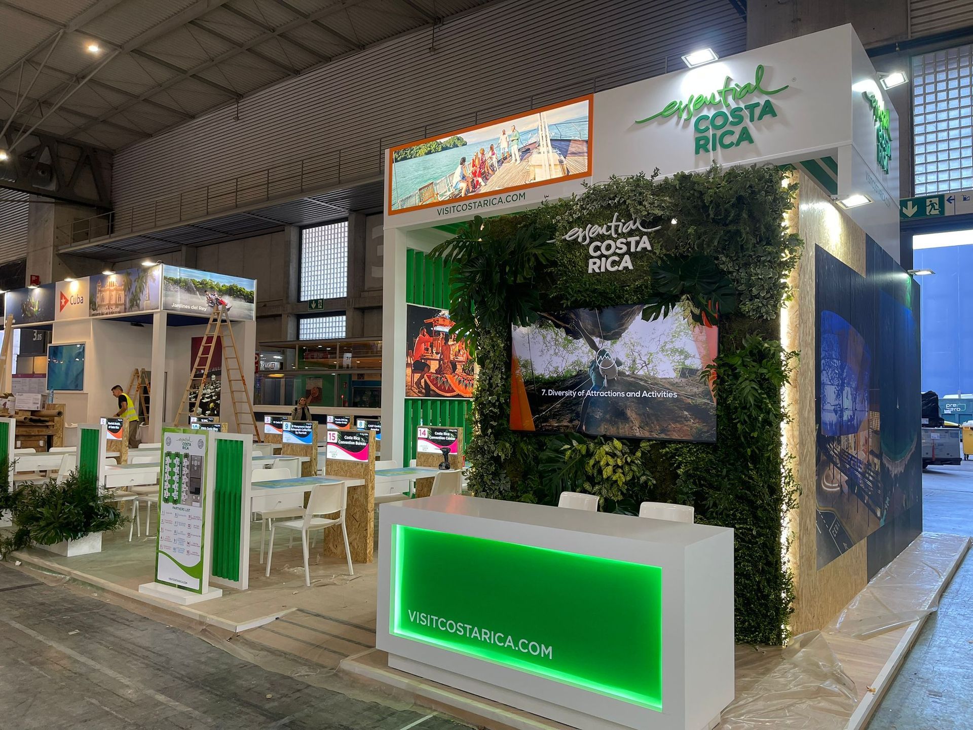 Stand de turismo de Costa Rica en una feria comercial; verde y blanco, con pantalla de video.