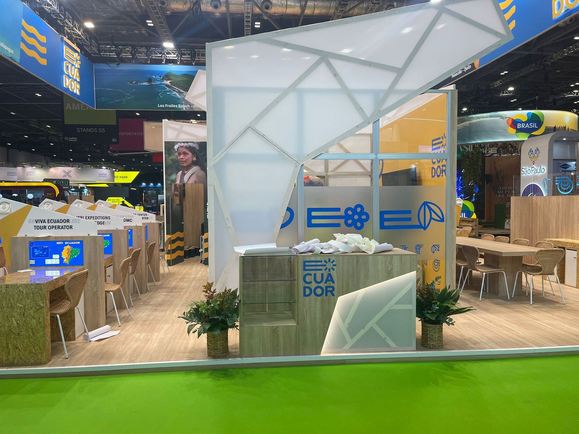 Stand de turismo de Ecuador con diseño geométrico blanco, logo azul, detalles en madera y mamparas de exhibición.