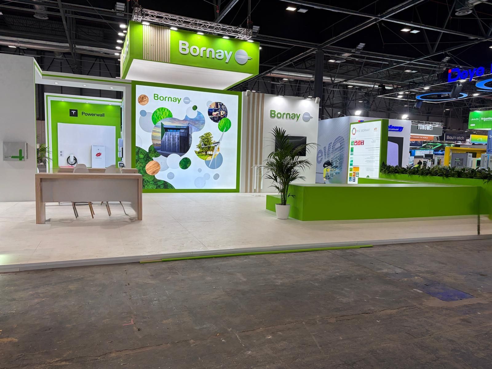 Stand de BornaY en una feria comercial. Marca verde y blanca. Pantalla central con productos. Rótulo luminoso.