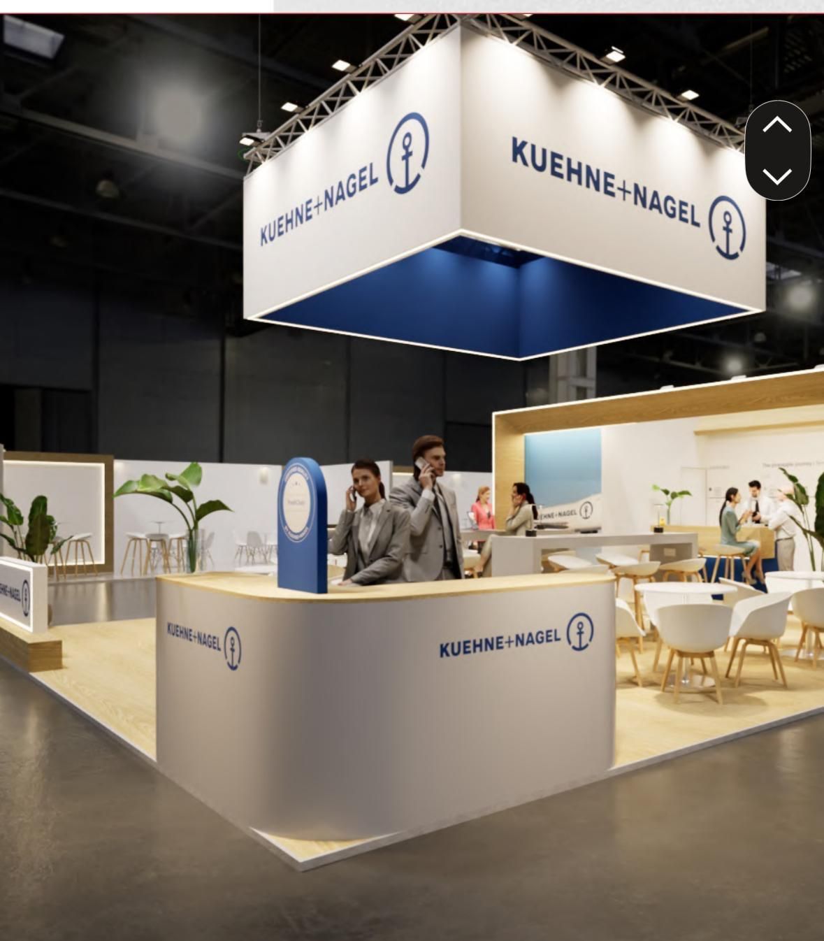 Stand de Kuehne + Nagel en una feria comercial con personal en un mostrador de recepción, marca azul y blanca, diseño moderno, interior.