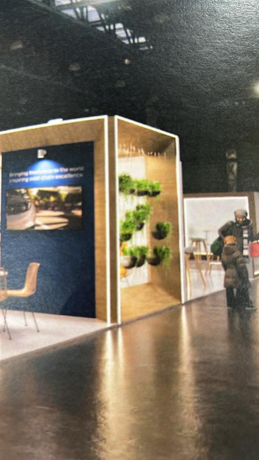 Stand de exposición con estructura de madera, plantas colgantes y una persona pasando.