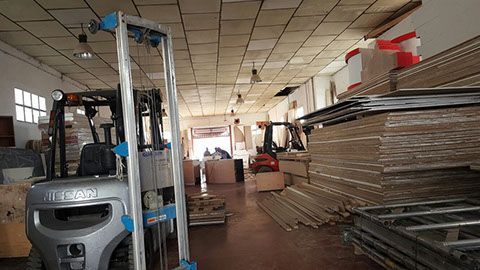 Interior de almacén con carretillas elevadoras, cajas y materiales de construcción.