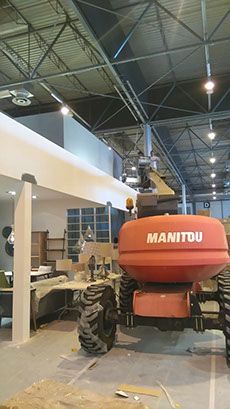 Manipulador telescópico Manitou de color naranja en un sitio de construcción, cerca de una viga blanca.