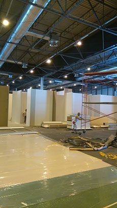 Gran sala de exposiciones inacabada con paredes temporales y trabajadores. Paredes blancas y marrones, andamios y suelo revestido.