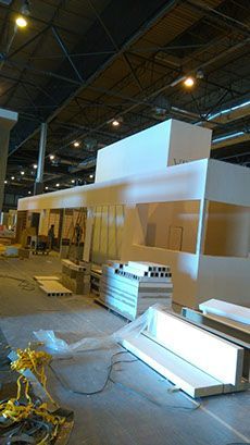 Stand blanco en construcción en un evento; pilas de materiales y herramientas en el suelo; entorno de almacén.
