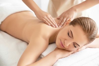 Zwei Personen erhalten eine Spa-Massage, eine liegt mit geschlossenen Augen auf einem Handtuch.