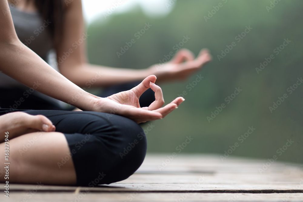 Menschen meditieren im Schneidersitz auf einer Holzterrasse im Freien, die Hände in einer Mudra-Pose.