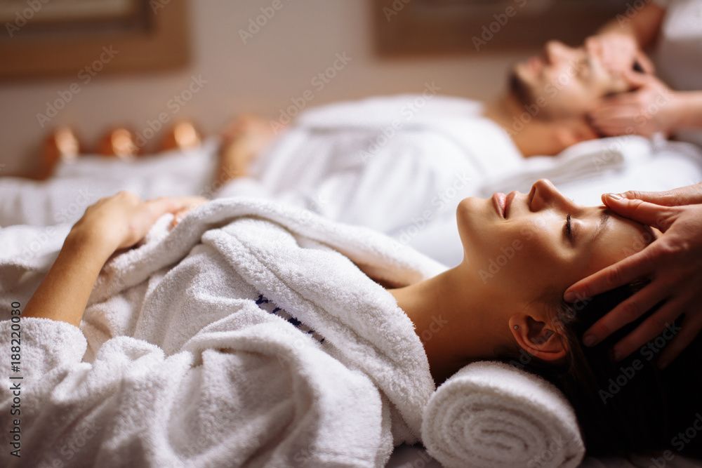 Zwei Personen erhalten eine Spa-Massage, eine liegt mit geschlossenen Augen auf einem Handtuch.