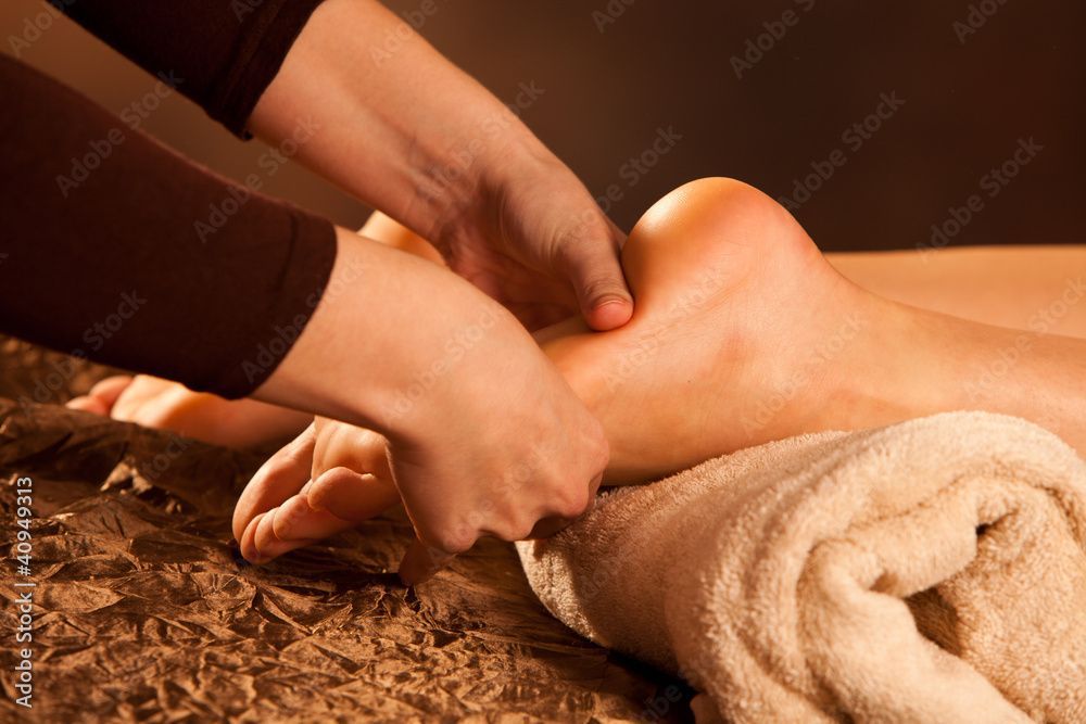 Hände massieren den Fuss einer Person auf einem Handtuch in einer warmen Spa-Umgebung