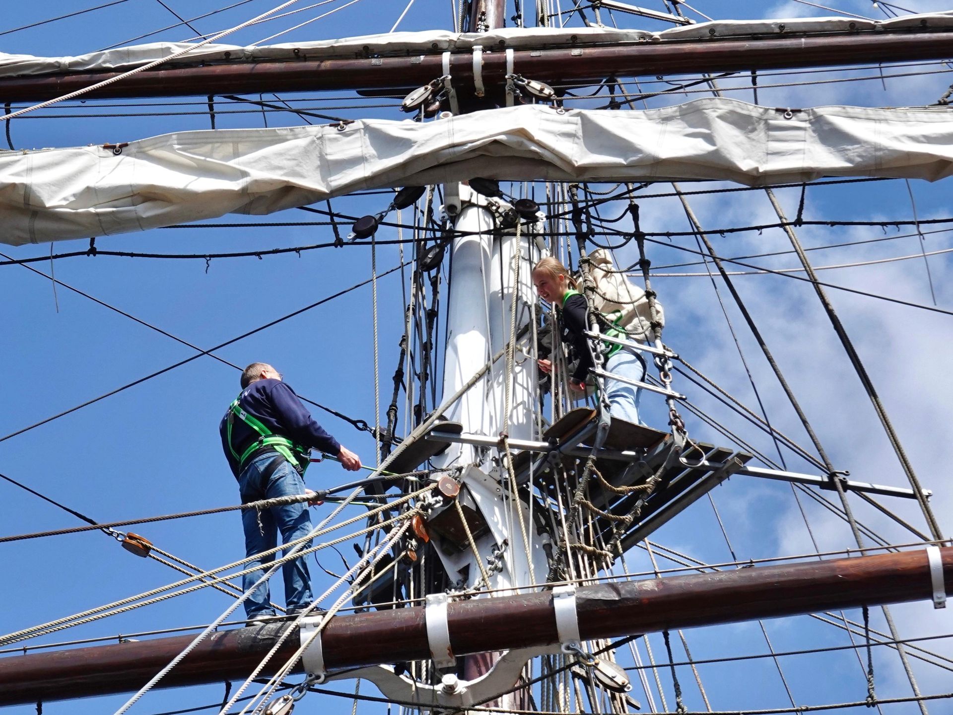 Zwei Personen klettern in die Takelagen eines Segelschiffs
