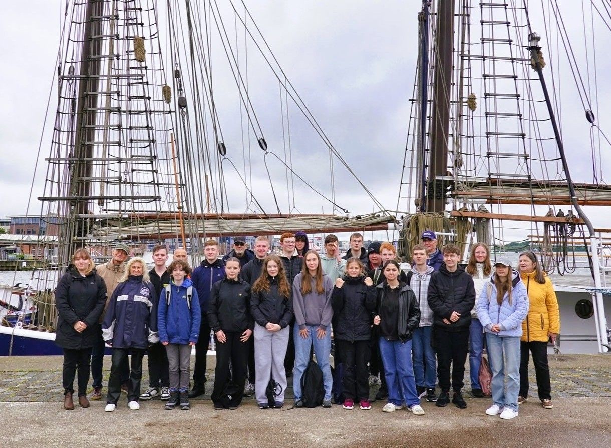 Eine Schulklasse steht vor einem Segelschiff