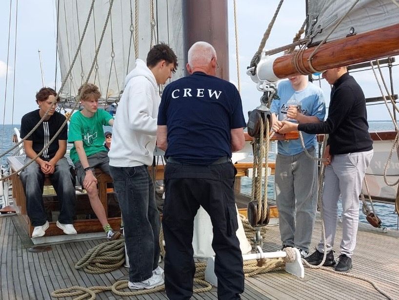 Eine Gruppe von Leuten setzt gemeinsam die Segel auf dem Deck eines Segelschiffs