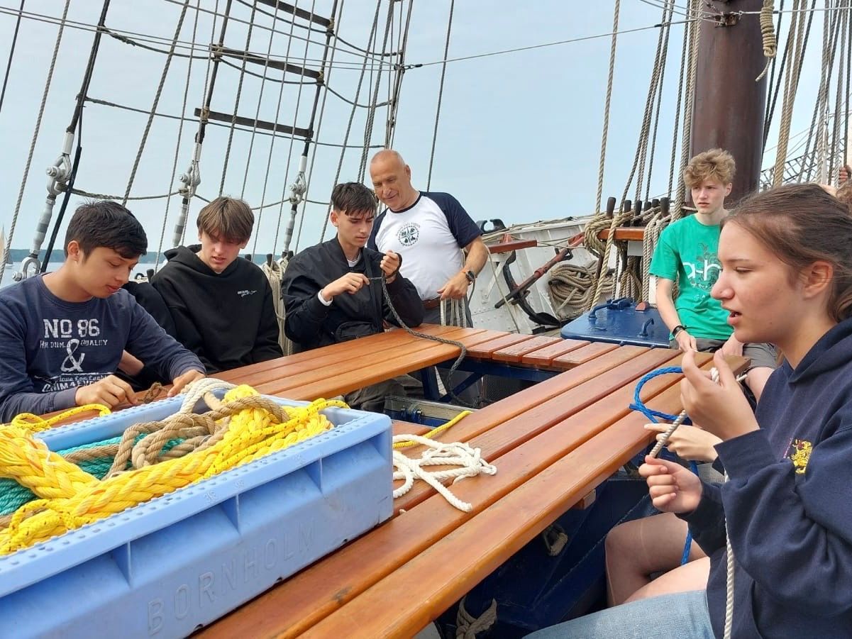 Eine Gruppe von Schülern übt die Seemannsknoten an Bord eines Segelschiffs