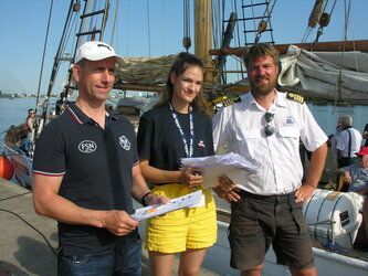 Drei Personen stehen nebeneinander auf einem Boot.