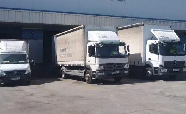 Tres camiones blancos están estacionados frente a un edificio.