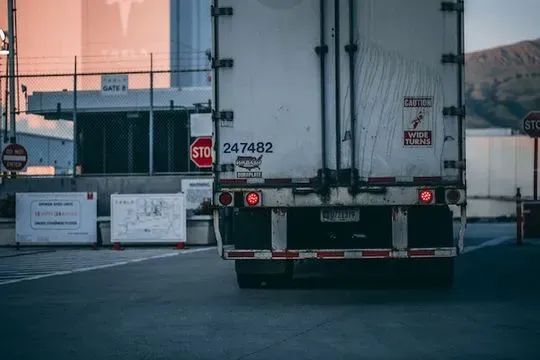 Un camión semirremolque blanco circula por una carretera al lado de una señal de pare.