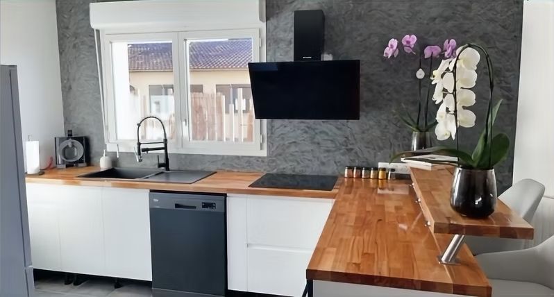 Cuisine moderne avec dosseret gris, armoires blanches, comptoirs en bois, électroménagers noirs et orchidées.